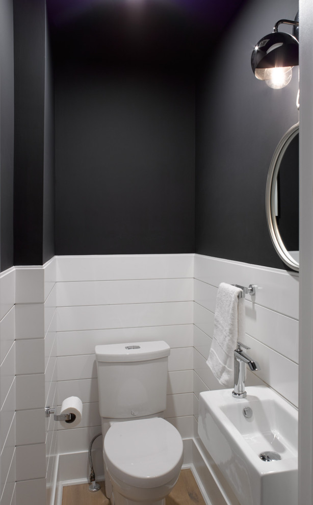 Photo of a small transitional powder room in Toronto with open cabinets, a two-piece toilet, black walls, light hardwood floors, a wall-mount sink and brown floor.