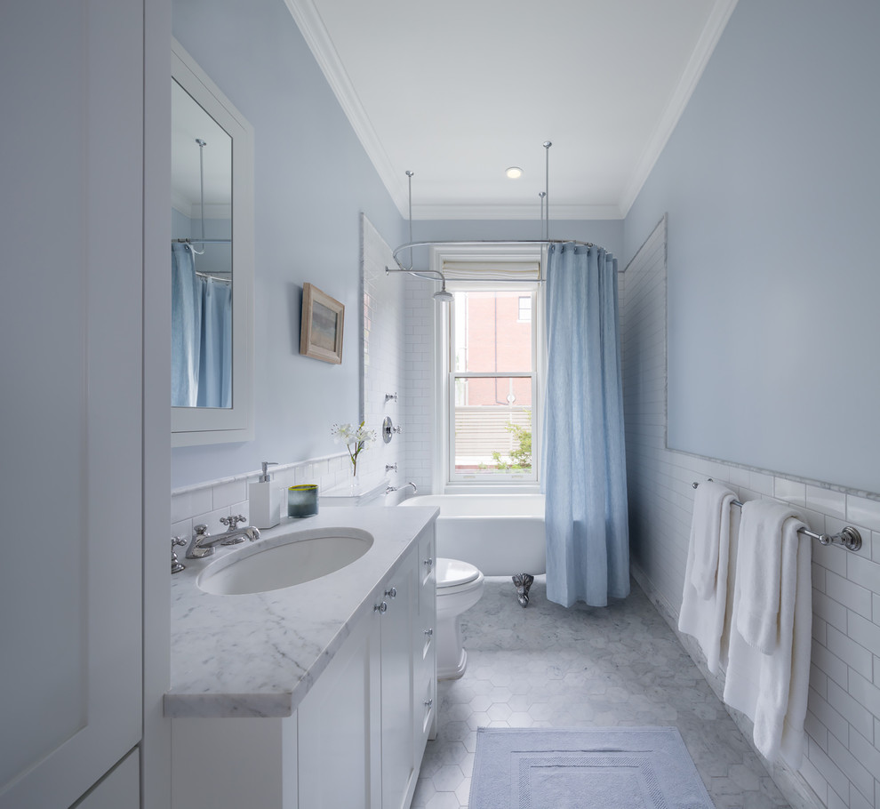 This is an example of a traditional bathroom in New York with an undermount sink, shaker cabinets, white cabinets, a claw-foot tub, a shower/bathtub combo, white tile, subway tile and blue walls.