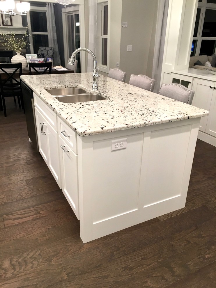 This is an example of an arts and crafts eat-in kitchen in Other with a double-bowl sink, recessed-panel cabinets, white cabinets, granite benchtops, stainless steel appliances, vinyl floors and with island.