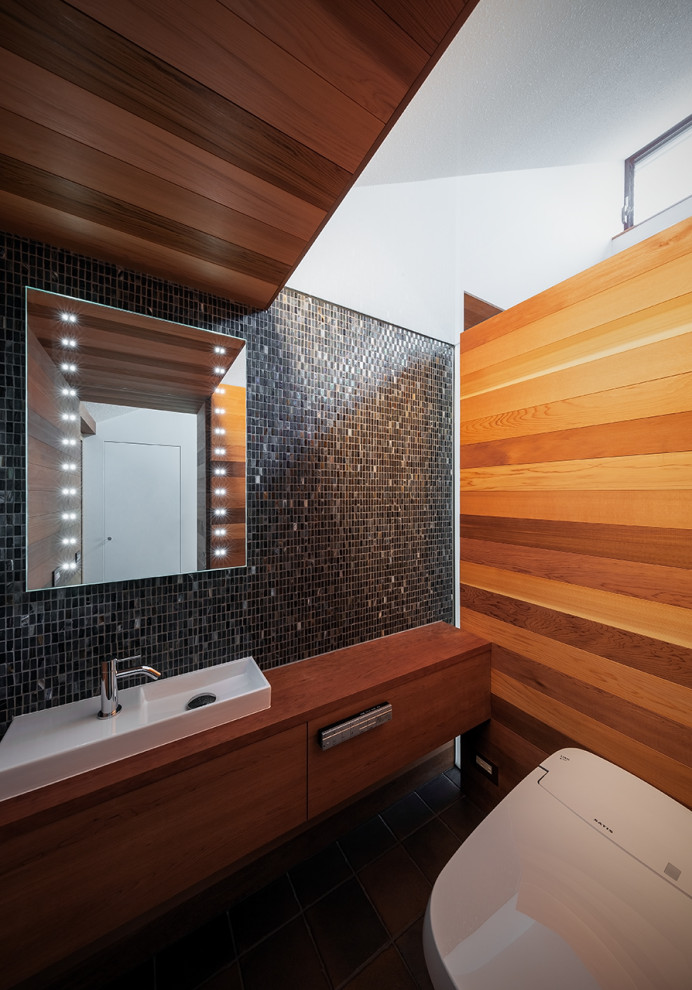 Photo of a powder room in Osaka with a one-piece toilet, ceramic floors, black floor, wood and wood walls.