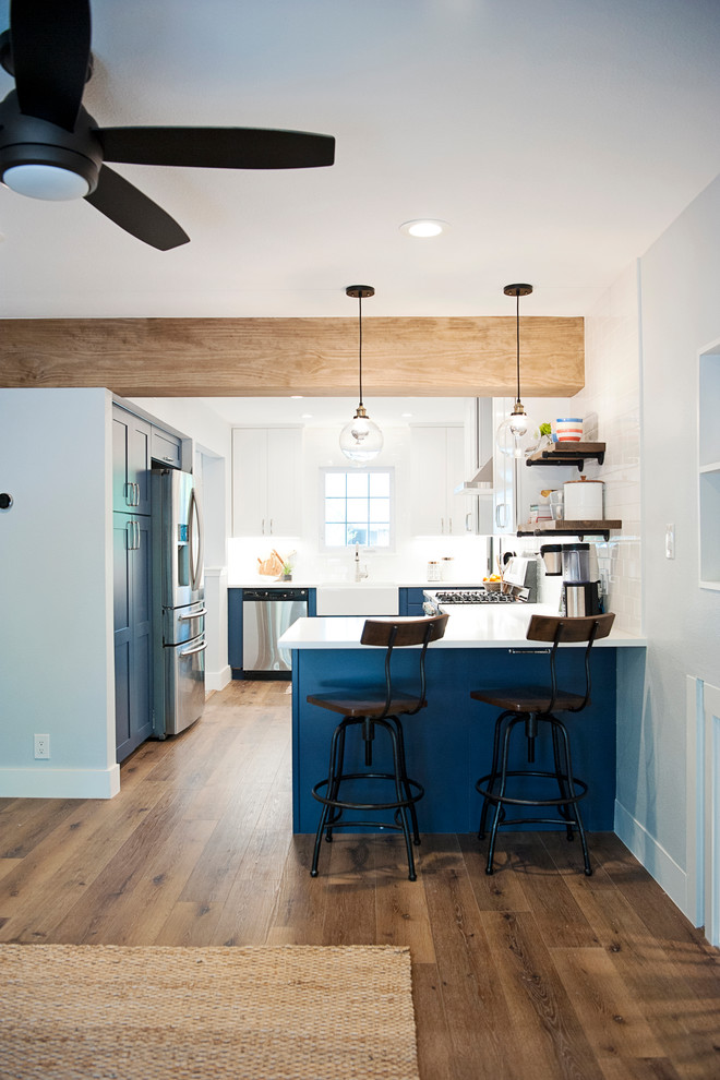 Inspiration for a mid-sized transitional vinyl floor and brown floor kitchen remodel in Austin with a farmhouse sink, shaker cabinets, blue cabinets, quartz countertops, white backsplash, ceramic backsplash, stainless steel appliances and white countertops