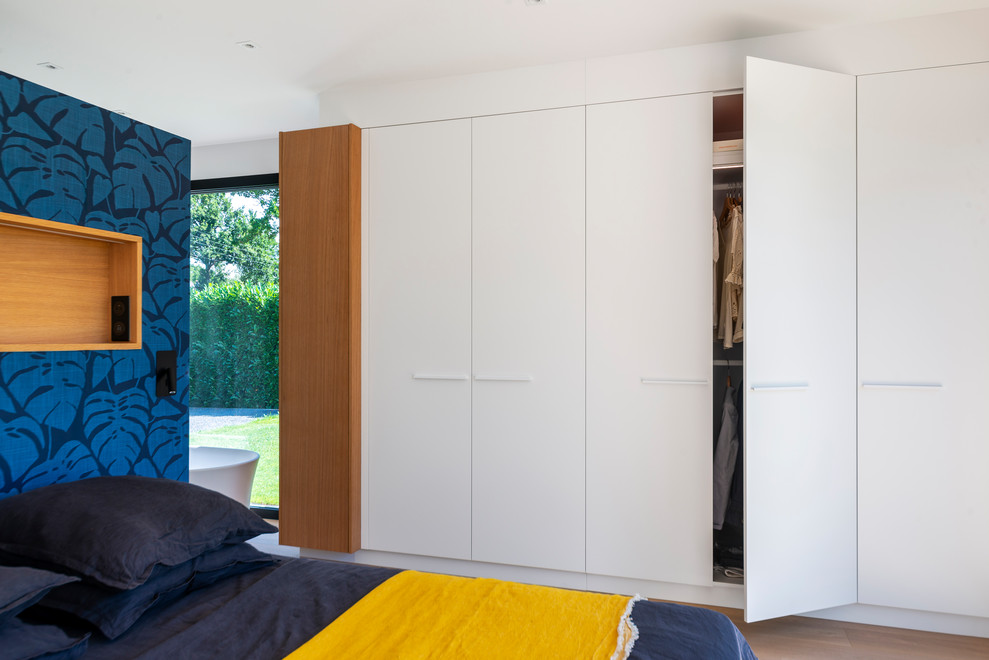 Large contemporary gender-neutral walk-in wardrobe in Nantes with beaded inset cabinets, white cabinets and light hardwood floors.