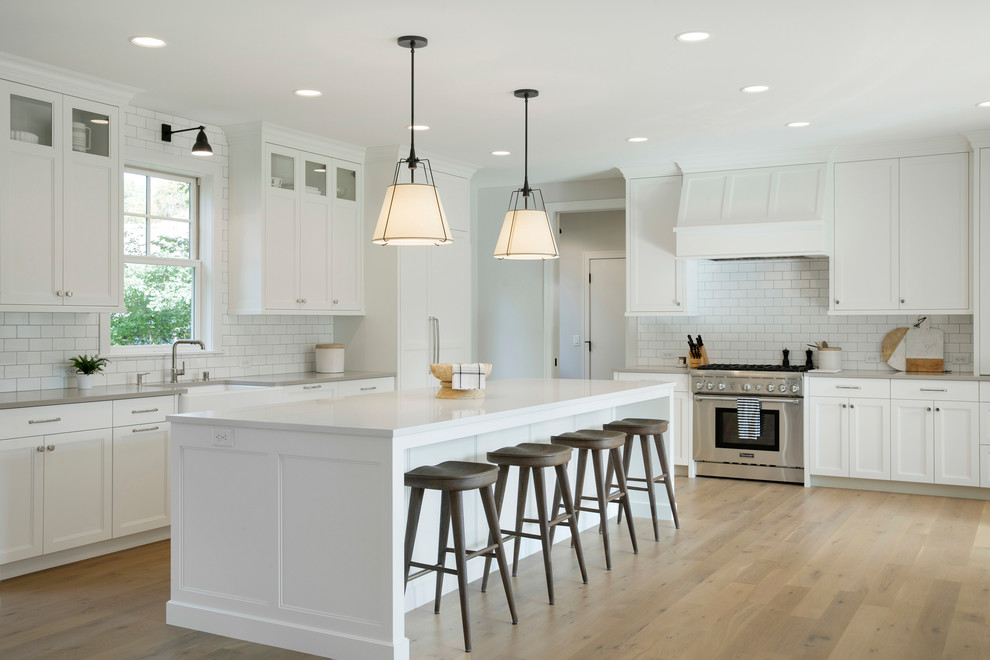 Design ideas for a country kitchen in Minneapolis with a farmhouse sink, shaker cabinets, white cabinets, white splashback, subway tile splashback, stainless steel appliances, light hardwood floors, with island, beige floor and grey benchtop.