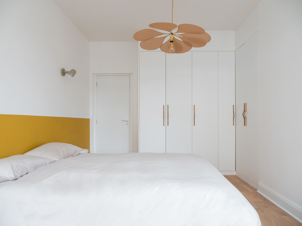 Idée de décoration pour une grande chambre parentale blanche et bois minimaliste avec un mur blanc, parquet clair, aucune cheminée, un sol marron et dressing.