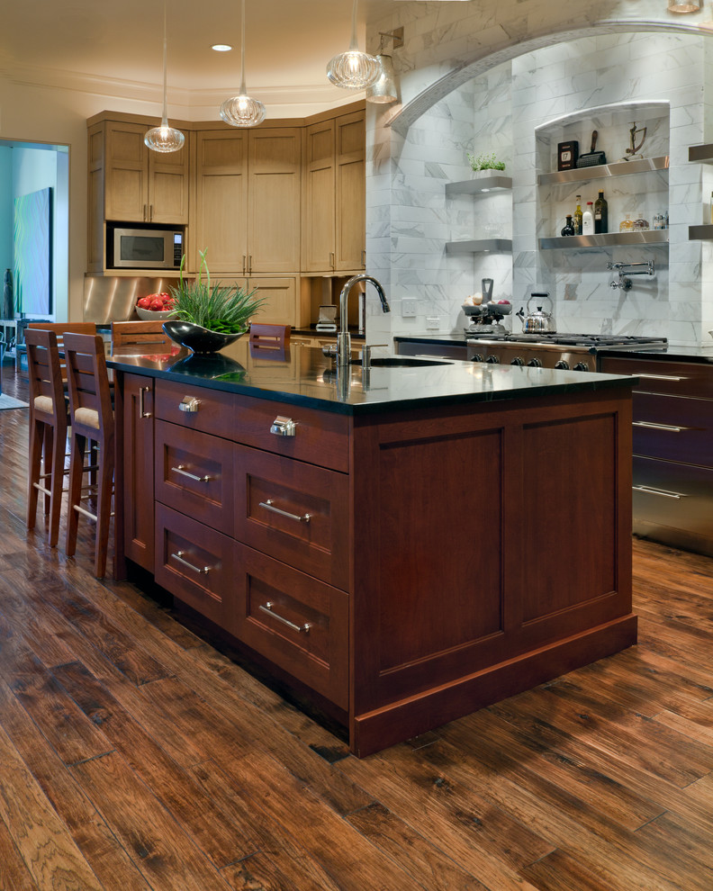 This is an example of a large modern u-shaped kitchen in Nashville with recessed-panel cabinets, stainless steel appliances, medium hardwood floors, with island, brown floor, light wood cabinets, multi-coloured splashback, black benchtop and a farmhouse sink.