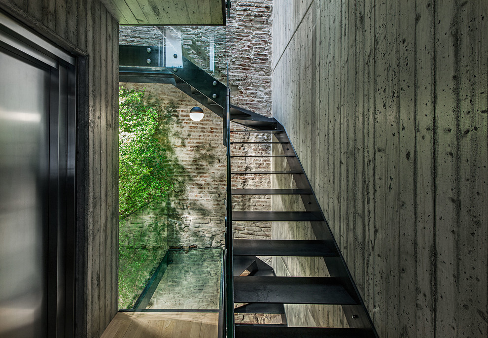 Inspiration for an industrial metal staircase in Milan with open risers and glass railing.
