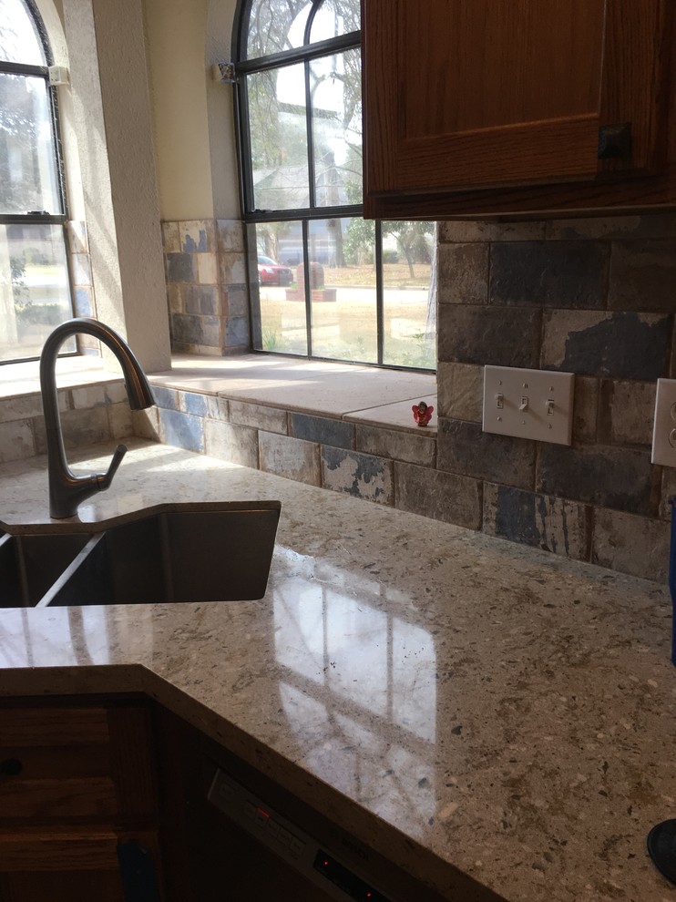 This is an example of a traditional kitchen in Houston with an undermount sink, recessed-panel cabinets, medium wood cabinets, quartz benchtops, multi-coloured splashback, stone tile splashback, stainless steel appliances, travertine floors, with island and beige floor.