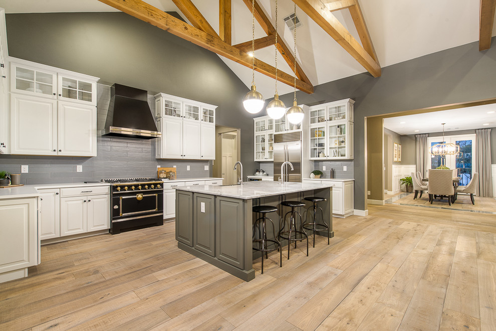 Inspiration for a large transitional light wood floor open concept kitchen remodel in Phoenix with a farmhouse sink, raised-panel cabinets, white cabinets, gray backsplash, glass tile backsplash, stainless steel appliances and an island