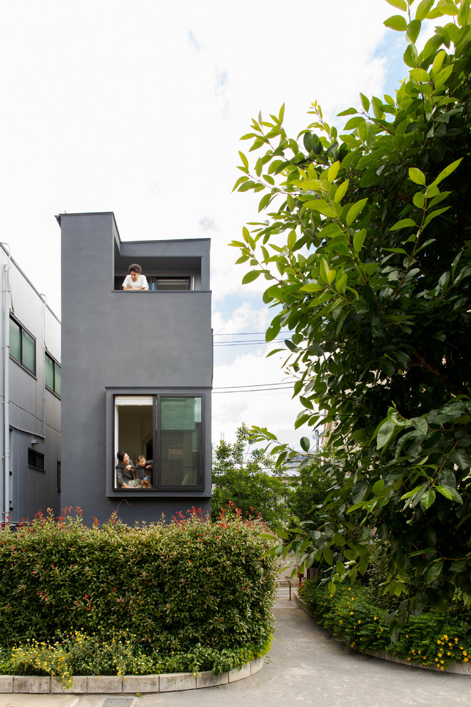 Small eclectic three-storey concrete black house exterior in Tokyo with a flat roof and a metal roof.