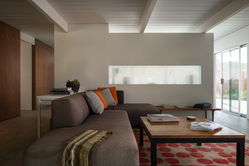 Inspiration for a mid-sized midcentury open concept living room in San Francisco with white walls, porcelain floors, a standard fireplace, a wall-mounted tv, grey floor and exposed beam.
