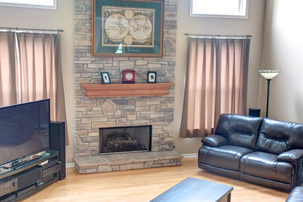 Photo of a mid-sized traditional open concept living room in Chicago with white walls, light hardwood floors, a standard fireplace, a stone fireplace surround, a wall-mounted tv and brown floor.