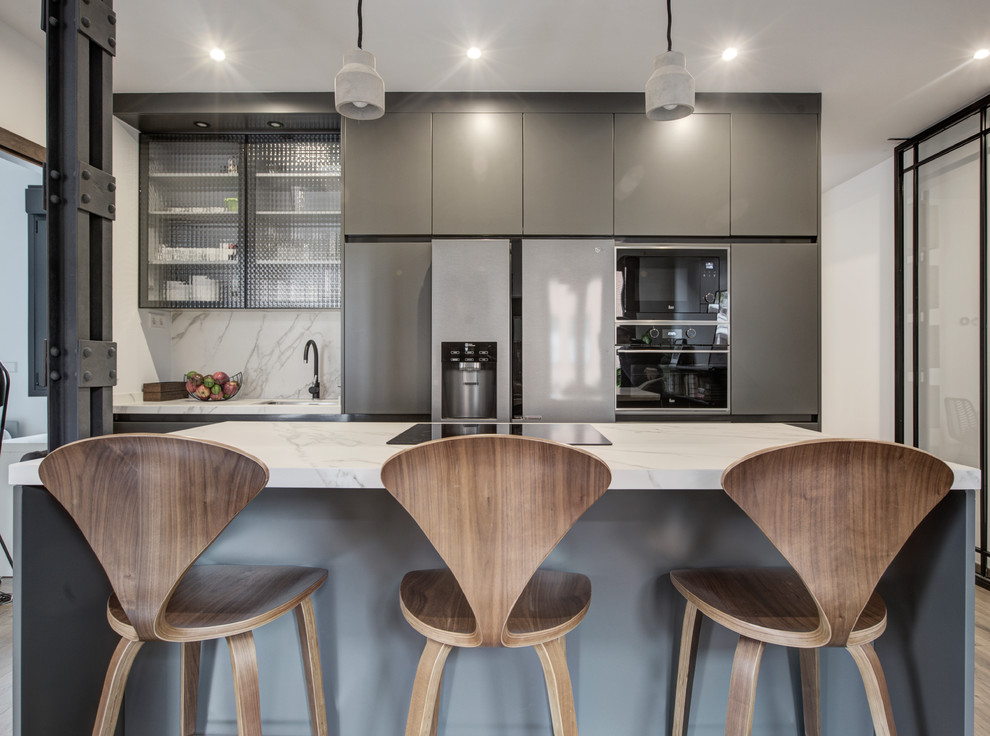 Photo of a mid-sized industrial open plan kitchen in Madrid with a single-bowl sink, glass-front cabinets, grey cabinets, marble benchtops, panelled appliances, laminate floors, with island, brown floor and white benchtop.