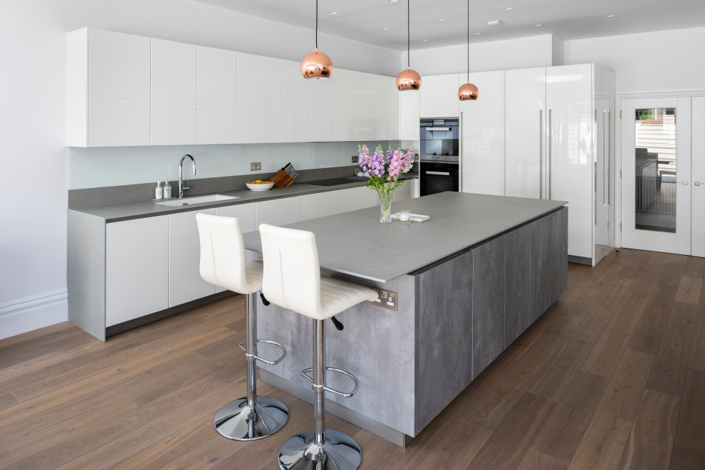 Photo of a large contemporary l-shaped open plan kitchen in Nice with a single-bowl sink, white cabinets, granite benchtops, white splashback, black appliances, with island, brown floor, grey benchtop, flat-panel cabinets, glass sheet splashback and dark hardwood floors.
