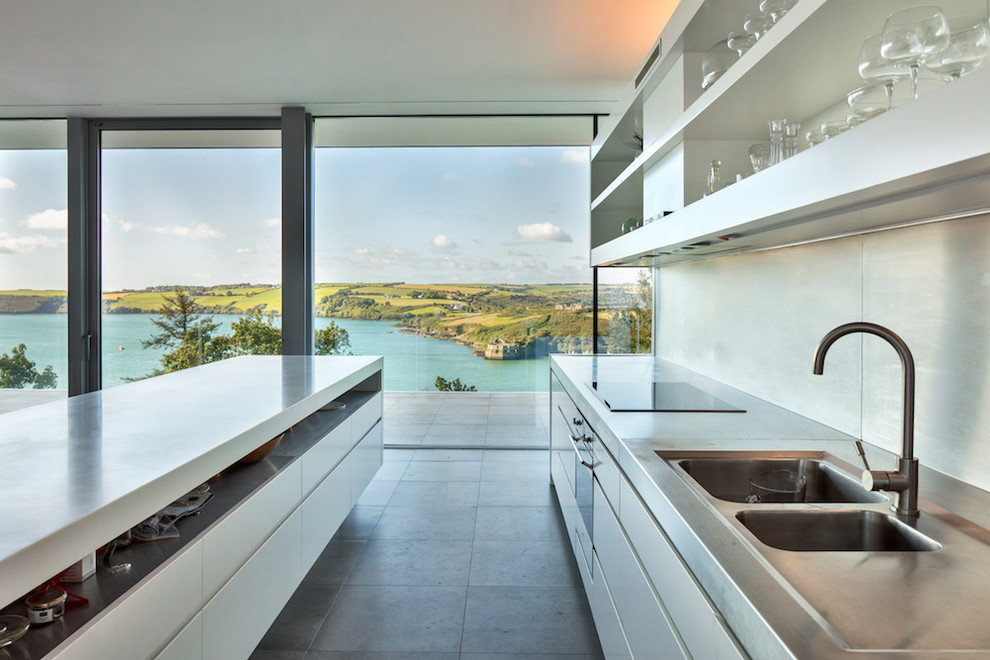 This is an example of a modern eat-in kitchen in Cork with a drop-in sink, open cabinets, white cabinets, stainless steel benchtops, grey splashback, stainless steel appliances, porcelain floors, with island, grey floor and white benchtop.