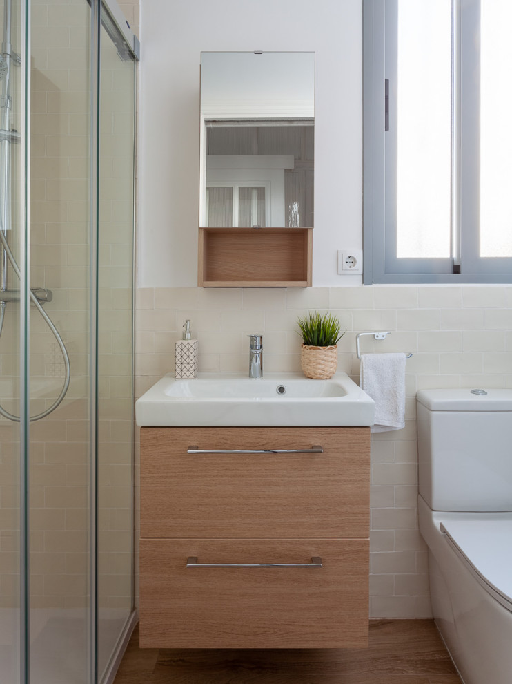 This is an example of a small contemporary 3/4 bathroom in Seville with beige tile, ceramic tile, ceramic floors, beige floor, a one-piece toilet, white walls, flat-panel cabinets, light wood cabinets, an alcove shower, an integrated sink, a sliding shower screen and white benchtops.