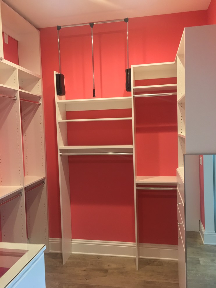 This is an example of a large modern women's walk-in wardrobe in Other with raised-panel cabinets, white cabinets, vinyl floors and brown floor.
