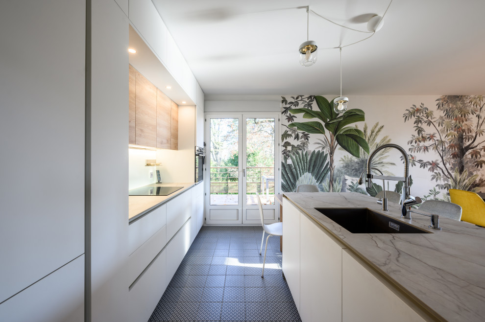 Mid-sized contemporary open plan kitchen in Lyon with an integrated sink, beaded inset cabinets, white cabinets, laminate benchtops, white splashback, panelled appliances, cement tiles, with island, green floor and grey benchtop.