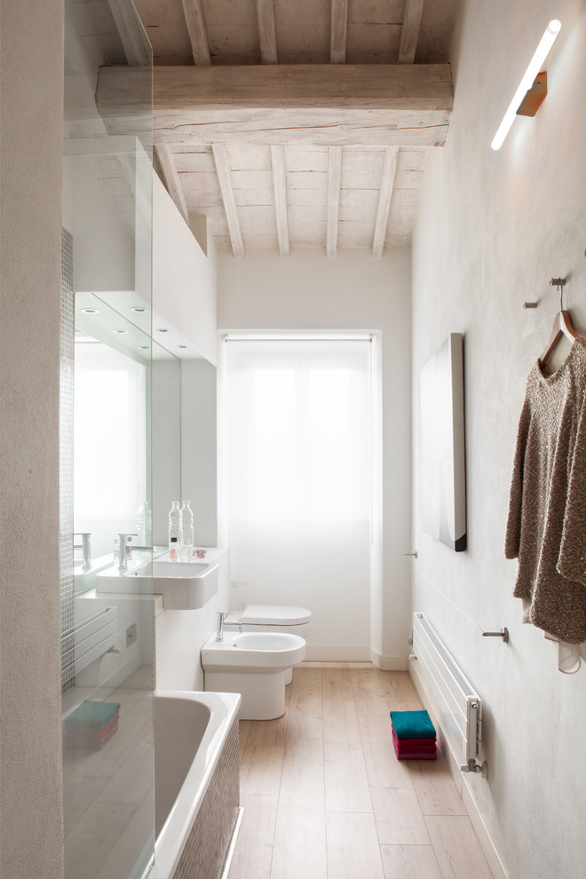 This is an example of a small scandinavian master bathroom in London with a vessel sink, white cabinets, a drop-in tub, a shower/bathtub combo, white walls, light hardwood floors and a bidet.