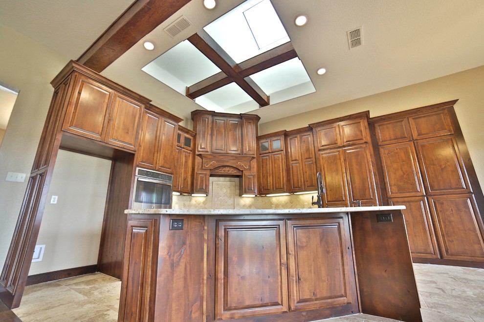 Mid-sized mountain style l-shaped porcelain tile eat-in kitchen photo in Dallas with an undermount sink, raised-panel cabinets, medium tone wood cabinets, granite countertops, beige backsplash, stone tile backsplash, stainless steel appliances and an island