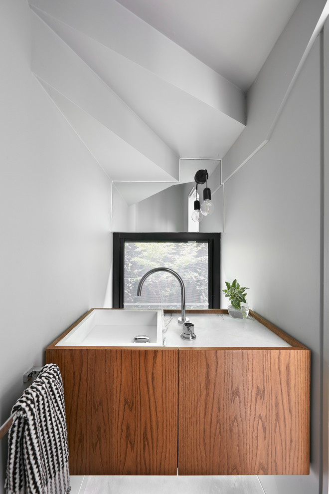 This is an example of a small contemporary 3/4 bathroom in Melbourne with furniture-like cabinets, brown cabinets, a wall-mount toilet, grey walls, concrete floors, a drop-in sink, marble benchtops, grey floor and white benchtops.