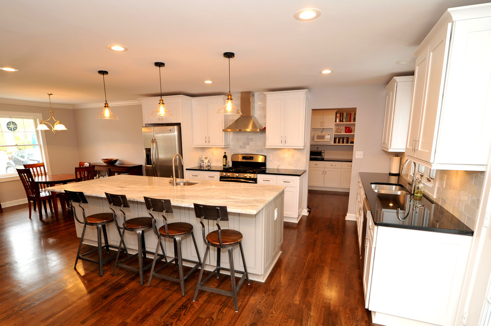 Example of a mid-sized transitional l-shaped medium tone wood floor open concept kitchen design in Atlanta with a double-bowl sink, white cabinets, quartzite countertops, white backsplash, stainless steel appliances and an island