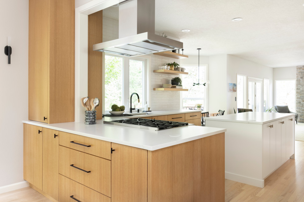 This is an example of a mid-sized contemporary u-shaped open plan kitchen in Portland with an undermount sink, flat-panel cabinets, medium wood cabinets, quartz benchtops, white splashback, cement tile splashback, stainless steel appliances, light hardwood floors, with island and white benchtop.