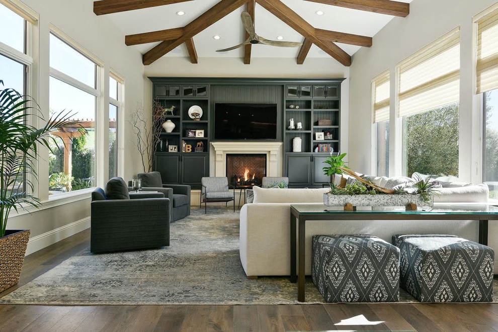 Design ideas for a mid-sized transitional open concept family room in San Francisco with beige walls, light hardwood floors, a standard fireplace, a wood fireplace surround, a wall-mounted tv and brown floor.