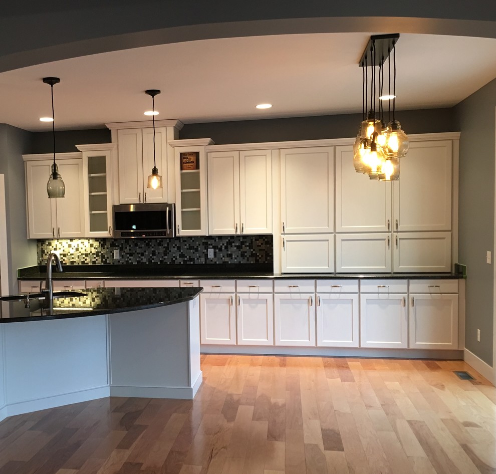 Large transitional l-shaped light wood floor eat-in kitchen photo with an undermount sink, recessed-panel cabinets, white cabinets, granite countertops, multicolored backsplash, glass tile backsplash, stainless steel appliances and an island