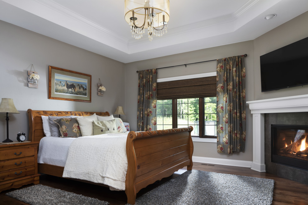 На фото: большая хозяйская спальня с серыми стенами, паркетным полом среднего тона, стандартным камином, фасадом камина из дерева, коричневым полом и кессонным потолком