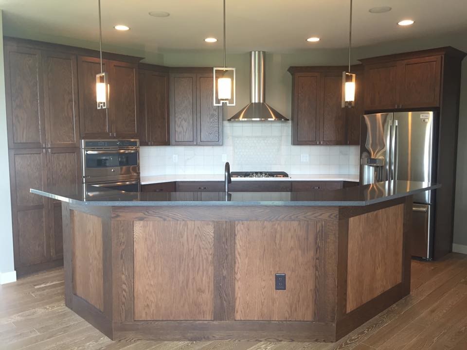 Large mountain style l-shaped dark wood floor and brown floor kitchen photo in Cedar Rapids with an undermount sink, shaker cabinets, dark wood cabinets, white backsplash, porcelain backsplash, stainless steel appliances and an island