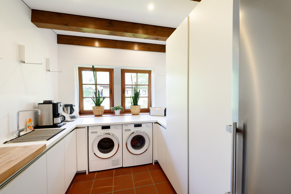 Design ideas for a small country u-shaped utility room in Essen with a drop-in sink, flat-panel cabinets, white cabinets, white walls, terra-cotta floors, a side-by-side washer and dryer, red floor and white benchtop.