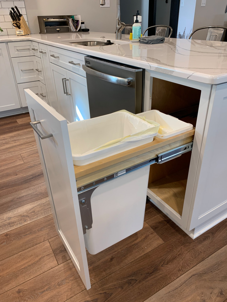 Example of a large transitional u-shaped vinyl floor and brown floor open concept kitchen design with an undermount sink, shaker cabinets, white cabinets, quartz countertops, white backsplash, ceramic backsplash, stainless steel appliances, an island and white countertops