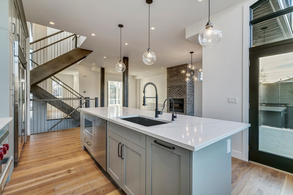 Example of a mid-sized transitional l-shaped medium tone wood floor and brown floor eat-in kitchen design in Calgary with a single-bowl sink, shaker cabinets, gray cabinets, quartzite countertops, white backsplash, ceramic backsplash, stainless steel appliances, an island and white countertops