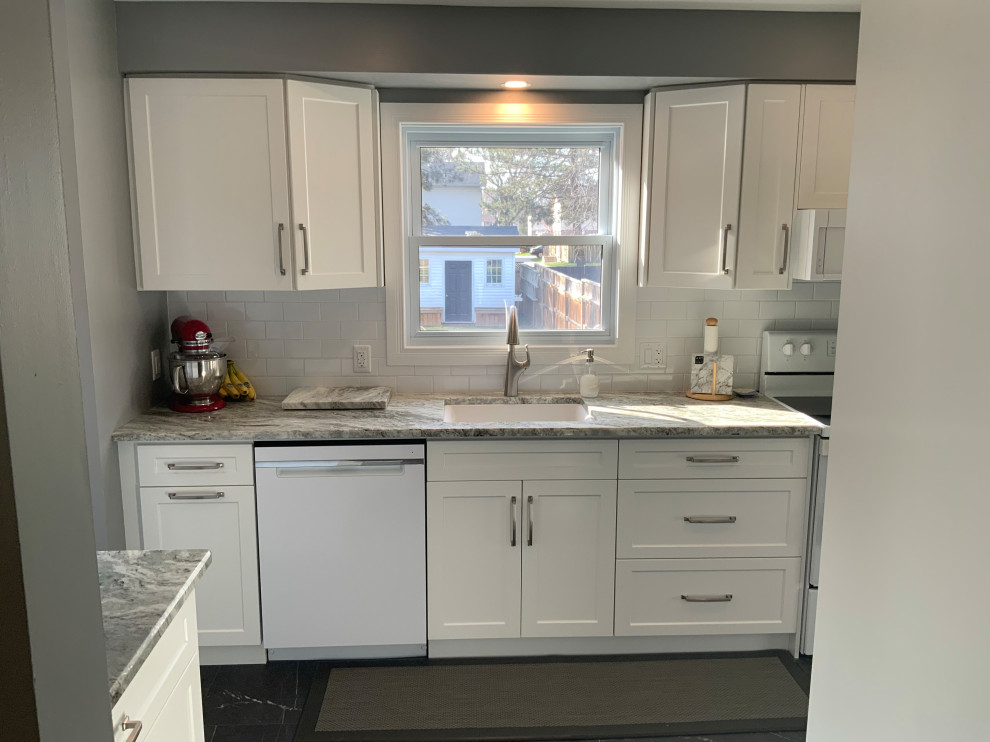 Small transitional galley laminate floor and gray floor kitchen pantry photo with an undermount sink, shaker cabinets, white cabinets, granite countertops, white backsplash, subway tile backsplash, white appliances, no island and white countertops