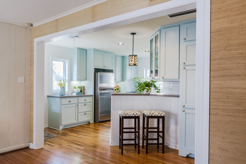 This is an example of a traditional u-shaped eat-in kitchen in Austin with a farmhouse sink, shaker cabinets, blue cabinets, white splashback, subway tile splashback, stainless steel appliances, no island, solid surface benchtops and medium hardwood floors.