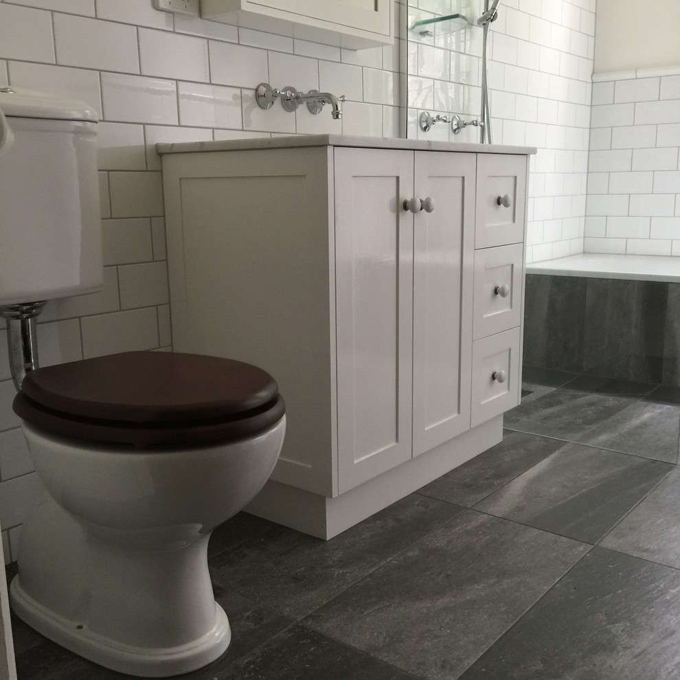 Photo of a small traditional master bathroom in Other with recessed-panel cabinets, white cabinets, a drop-in tub, an open shower, a two-piece toilet, white tile, ceramic tile, white walls, porcelain floors, an undermount sink, marble benchtops, grey floor and an open shower.
