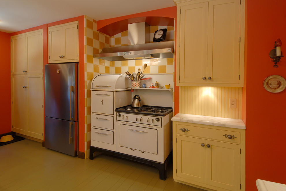 Photo of a mid-sized eclectic l-shaped separate kitchen in San Francisco with white appliances, yellow cabinets, timber splashback, an undermount sink, shaker cabinets, marble benchtops, yellow splashback, painted wood floors, a peninsula and beige floor.