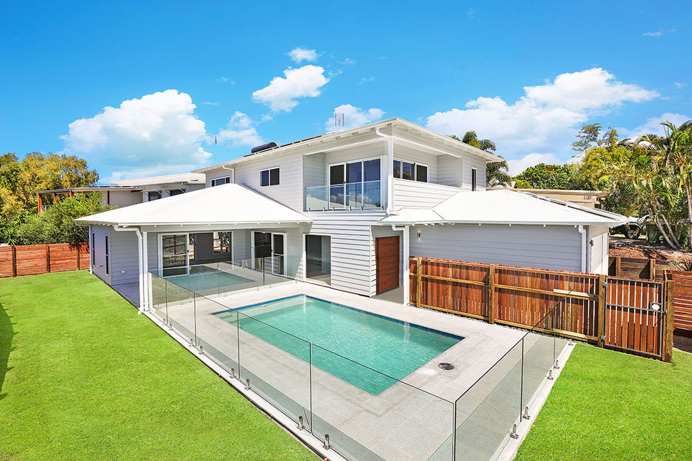This is an example of a mid-sized beach style two-storey grey house exterior in Sunshine Coast with concrete fiberboard siding, a hip roof and a metal roof.