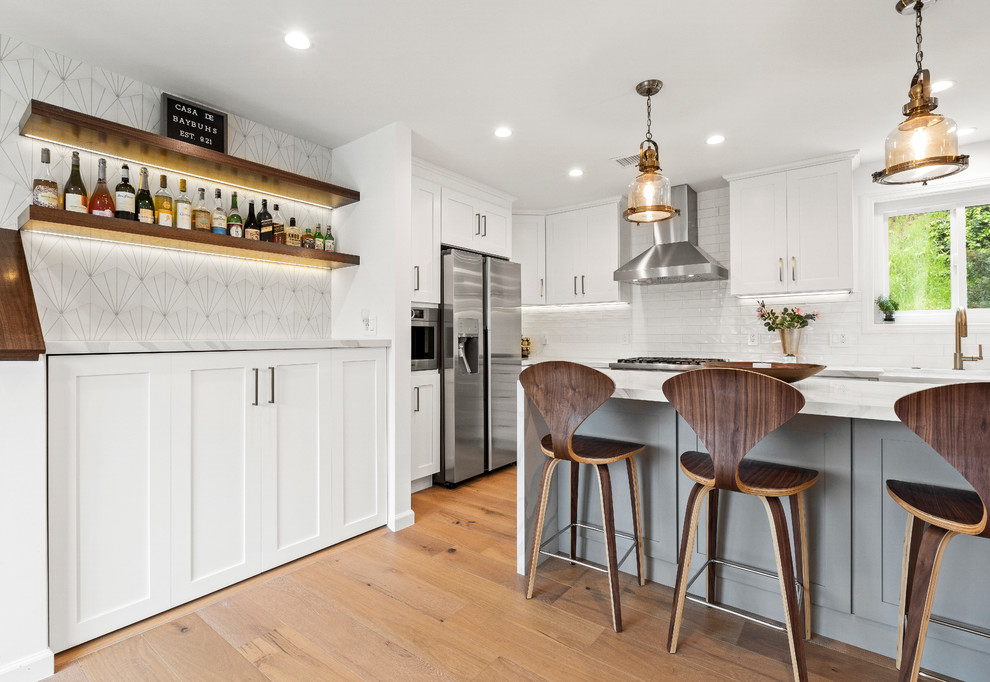 Inspiration for a mid-sized transitional home bar in Los Angeles with shaker cabinets, white cabinets, quartz benchtops, white splashback, light hardwood floors, brown floor, cement tile splashback and white benchtop.