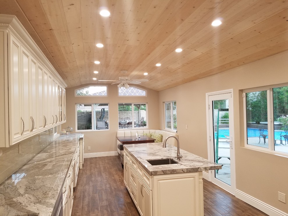 Large modern l-shaped separate kitchen in Los Angeles with an undermount sink, raised-panel cabinets, white cabinets, granite benchtops, beige splashback, glass tile splashback, stainless steel appliances, dark hardwood floors, with island and brown floor.