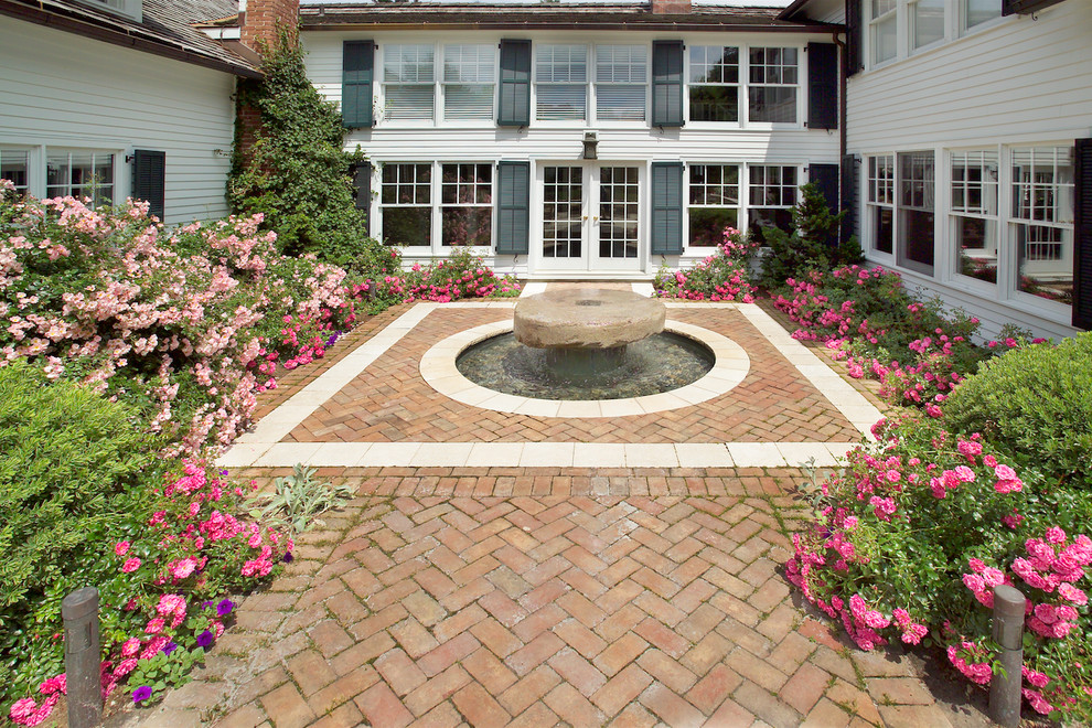 Design ideas for a mid-sized traditional courtyard patio in New York with a water feature, brick pavers and no cover.