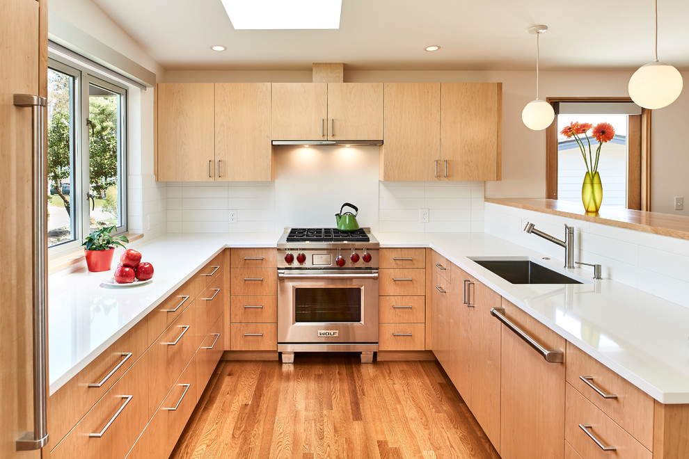 Design ideas for a mid-sized midcentury u-shaped kitchen in Seattle with an undermount sink, flat-panel cabinets, light wood cabinets, white splashback, subway tile splashback, panelled appliances, medium hardwood floors, white benchtop, a peninsula and brown floor.