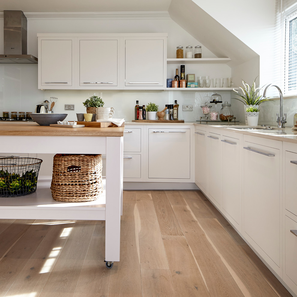 Inspiration for a country l-shaped kitchen in London with an undermount sink, flat-panel cabinets, white cabinets, wood benchtops, stainless steel appliances, light hardwood floors and with island.