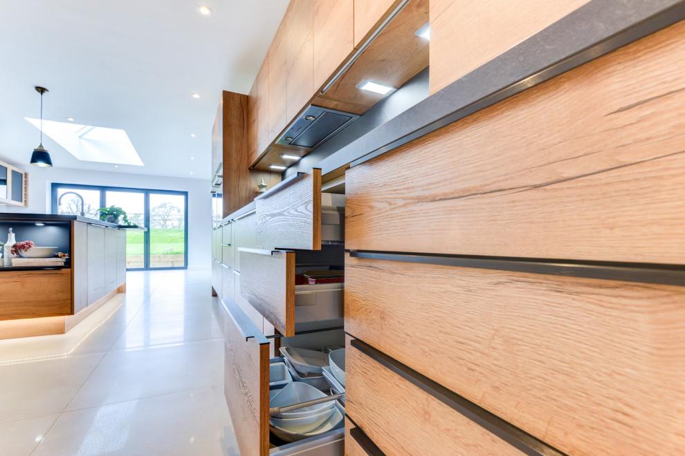 This is an example of a large contemporary galley open plan kitchen in Sussex with an integrated sink, flat-panel cabinets, medium wood cabinets, laminate benchtops, grey splashback, panelled appliances, porcelain floors, with island, white floor and grey benchtop.