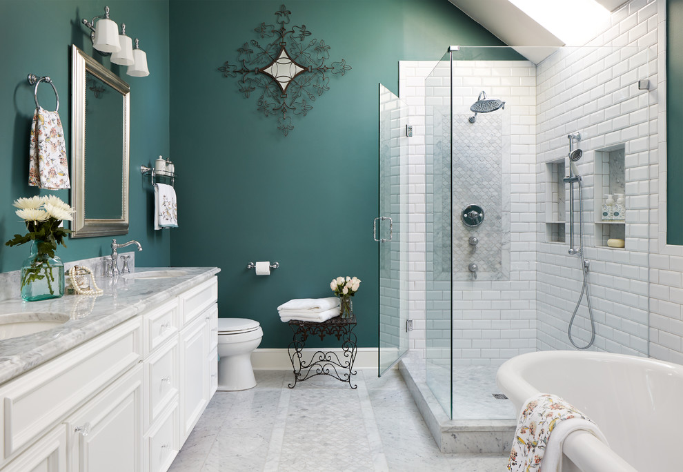 This is an example of a mid-sized traditional master bathroom in Chicago with raised-panel cabinets, white cabinets, a freestanding tub, a corner shower, a one-piece toilet, white tile, ceramic tile, green walls, marble floors, an undermount sink, marble benchtops, grey floor, a hinged shower door and grey benchtops.
