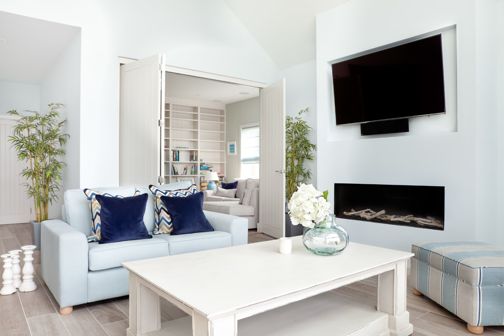 Inspiration for an expansive beach style open concept living room in Gloucestershire with blue walls, light hardwood floors, a plaster fireplace surround, a wall-mounted tv, grey floor and a ribbon fireplace.
