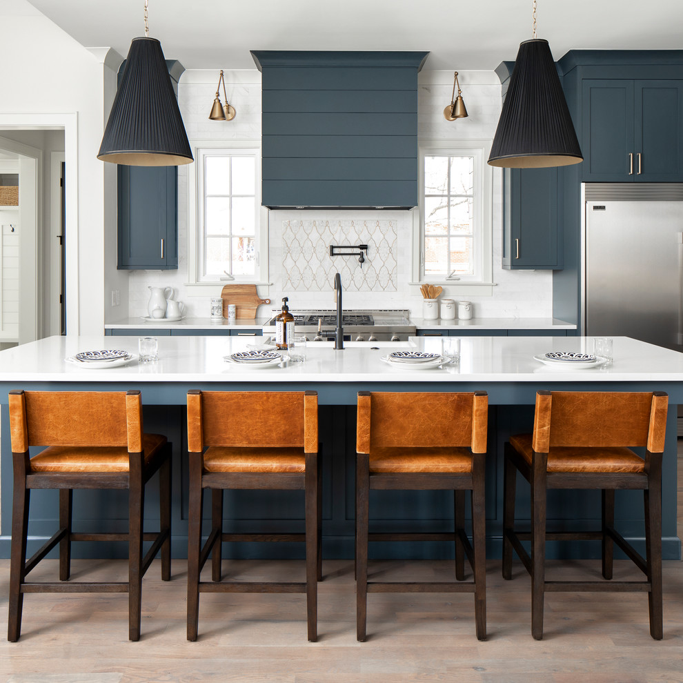 Large country l-shaped eat-in kitchen in Charlotte with a farmhouse sink, recessed-panel cabinets, blue cabinets, quartz benchtops, white splashback, subway tile splashback, stainless steel appliances, medium hardwood floors, with island, brown floor and white benchtop.