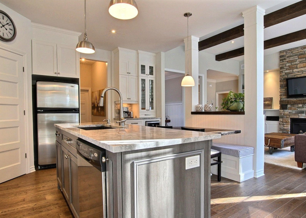 This is an example of a mid-sized traditional u-shaped eat-in kitchen in Montreal with an undermount sink, shaker cabinets, white cabinets, granite benchtops, grey splashback, stone slab splashback, stainless steel appliances, medium hardwood floors, with island, brown floor, grey benchtop and exposed beam.