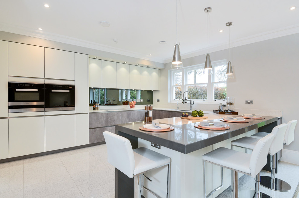 Design ideas for a mid-sized modern u-shaped eat-in kitchen in Berkshire with a drop-in sink, flat-panel cabinets, white cabinets, quartzite benchtops, grey splashback, mirror splashback, panelled appliances and a peninsula.