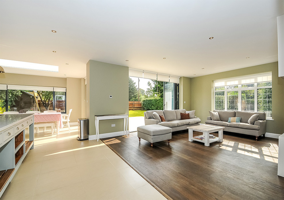 Photo of a large transitional open concept living room in London with green walls, no fireplace, a built-in media wall, medium hardwood floors and brown floor.